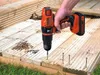 A person is using a Black & Decker cordless drill to screw a deck board into place. There are screws and drill bits on the deck. Produktbild-Vorschau