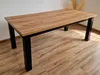 A wooden dining table with black legs is shown in a room with wooden flooring. Produktbild-Vorschau