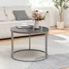 A round coffee table with a marble top and metal legs is placed on a rug in front of a sofa. A vase with dried flowers and a book with a cup of tea are on the table. Produktbild-Vorschau