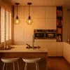 A modern kitchen with pendant lights, built-in ovens, and a kitchen island with stools. Produktbild-Vorschau