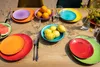 A table set with colorful plates, fruit, and glasses. Produktbild-Vorschau