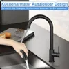 A hand is using a black kitchen faucet with a pull-down sprayer over a sink, with a cutting board and fruit in the background. Anteprima dell’immagine prodotto