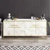 A white and gold sideboard with marble-like detailing, set against a dark, ribbed wall and a patterned rug. Náhled obrázku produktu
