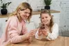 A woman and a girl are sitting at a wooden table, looking at a wooden model of a fish. Podgląd zdjęcia produktu