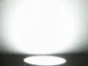 A white LED lamp is shown on a dark surface with a bright white light emanating from it onto a white wall. Náhled obrázku produktu