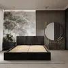 A modern bedroom with a black upholstered bed, a large mural on the wall, and a round mirror. Produktbild-Vorschau