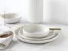 A set of white ceramic dishes and chopsticks arranged on a white tablecloth, with a dried plant sprig in the foreground and a ribbed vase in the background. Produktbild-Vorschau