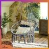 A hanging chair with pillows in a room with patterned wallpaper and a plant. Voir les images du produit
