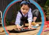 A young child is drawing with crayons on a piece of black paper on a wooden deck. Voir les images du produit