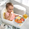 A baby sitting in a high chair with a plate of food in front of her. Produktbild-Vorschau