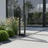 A modern outdoor pathway light is shown in a garden setting with lush greenery and paving stones. Náhľad obrázku produktu