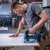 A man is using a jigsaw to cut a piece of material in a workshop. Anteprima dell’immagine prodotto