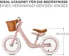 A pink balance bike with a brown basket and seat, shown against a white background with text overlays indicating features and dimensions. Produktbild-Vorschau