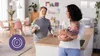 A family in a kitchen setting, with a man holding a baby bottle and a woman holding a baby. Produktbild-Vorschau