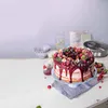 A decorated cake with berries and chocolate drizzle on a cake stand, with baking accessories in the background. Produktbild-Vorschau