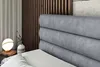 A close-up view of a gray upholstered headboard of a bed, with a bedside table and lamp visible on the left. Produktbild-Vorschau