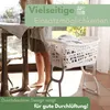 A person is ironing clothes next to a laundry basket on a stand. Produktbild-Vorschau