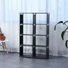 A black multi-layer shelf unit is shown in a room with a white curtain in the background and a plant on the right side. A small guitar is on a chair on the left. Produktbild-Vorschau