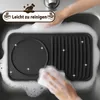 Hands washing a black raclette grill in a sink filled with soapy water. Náhľad obrázku produktu