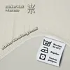 A close-up of a beige fabric product, likely a fitted sheet, with text and care symbols. Produktbild-Vorschau