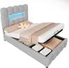A grey upholstered bed with storage, showing the mattress lifted to reveal the storage compartment underneath. The headboard has integrated blue LED lighting. Náhled obrázku produktu