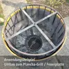 A modified metal barrel, possibly for a fire pit or grill, sits outdoors on a paved surface. Anteprima dell’immagine prodotto