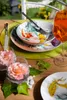 A table setting with plates, bowls, cutlery, flowers, and a drink. Podgląd zdjęcia produktu