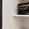 A close-up view of folded clothes on a white shelf inside a closet. Produktbild-Vorschau