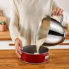 A person is pouring batter from a mixing bowl into a red cake pan. Produktbild-Vorschau