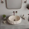 A bathroom sink area with a stone-like basin, faucet, mirror, and accessories. Produktbild-Vorschau