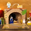 A wooden nativity scene with figures and a stable, set against a warm, wooden background with a red candle and a gift box. Produktbild-Vorschau