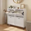 A white shoe cabinet with open doors displaying shoes, placed in a hallway with an umbrella stand and a mirror on the wall. Náhľad obrázku produktu