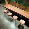 A long wooden table with four stools in front of a window with greenery outside. Produktbild-Vorschau