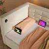A beige sofa bed with two tablets charging on it, connected to a USB port on the side of the sofa. Produktbild-Vorschau