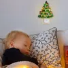 A baby sleeping next to a decorative Christmas tree night light plugged into the wall. Náhľad obrázku produktu