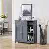 A gray cabinet with doors and shelves, decorated with a lamp, a clock, a figurine, and books. An umbrella stand with umbrellas is next to it. Produktbild-Vorschau