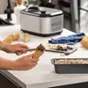 A person is scooping chocolate ice cream into a cone next to an ice cream maker and other ingredients. Produktbild-Vorschau