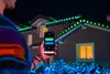 A person is holding a smartphone and controlling outdoor Christmas lights on a house at night. Podgląd zdjęcia produktu