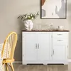A white sideboard with a brown top is shown in a dining room setting, with a chair and table cloth visible on the left, and a painting on the wall behind it. Produktbild-Vorschau