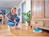 A woman is mopping a wooden floor in a room with furniture and plants. Anteprima dell’immagine prodotto