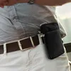 A person wearing a grey shirt and white pants, with a brown belt and a black phone pouch attached to the belt. Produktbild-Vorschau