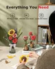 A person is assembling a 3D wooden flower craft kit on a table, with finished bouquets in the background. Produktbild-Vorschau