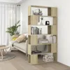 A bookshelf room divider is shown in a living room setting, next to a sofa and a window with curtains. Produktbild-Vorschau