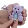 A hand holding a small purple teddy bear toy with a bottle. Anteprima dell’immagine prodotto