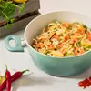 A close-up shot of a teal pot filled with zucchini noodles, shrimp, and lemon slices, with red chili peppers in the foreground. Produktbild-Vorschau