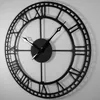 A black metal clock with Roman numerals on a white wall. Voir les images du produit