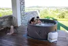 A couple relaxing in a hot tub on a wooden deck with a scenic view. Produktbild-Vorschau