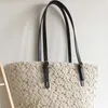 A close-up of a beige crocheted tote bag with black leather handles, hanging against a light gray wall. Produktbild-Vorschau