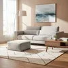 A modern living room with a sofa, ottoman, coffee table, rug, and artwork. Produktbild-Vorschau