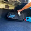 A person's hand is placing an item into a black trunk organizer in the trunk of a car. Náhled obrázku produktu
